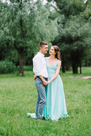 happy guy in a white shirt and a girl in a turquoise dress, the bride and groom are walking in the forest parkの写真素材