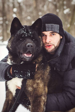 A man in a jacket and a knitted hat walks through a snowy forest with an American Akita dogの写真素材