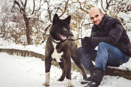A man in a jacket and a knitted hat walks through a snowy forest with an American Akita dogの写真素材