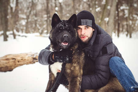 A man in a jacket and a knitted hat walks through a snowy forest with an American Akita dogの写真素材