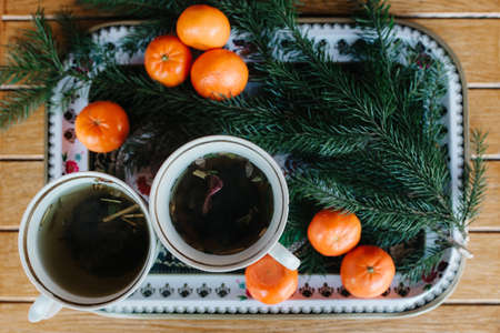two cups of herbal tea on a table with tangerines and a spruce branch on christmas eveの写真素材