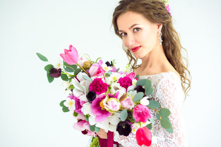 joyful girl bride in a white knitted dress posing with a bouquet of flowers in the studio on a white backgroundの写真素材
