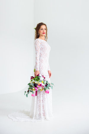 joyful girl bride in a white knitted dress posing with a bouquet of flowers in the studio on a white backgroundの写真素材