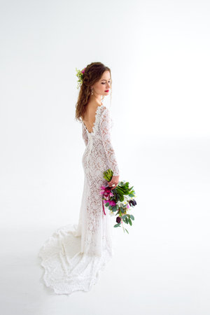 joyful girl bride in a white knitted dress posing with a bouquet of flowers in the studio on a white backgroundの写真素材