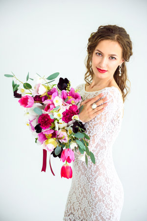 joyful girl bride in a white knitted dress posing with a bouquet of flowers in the studio on a white backgroundの写真素材