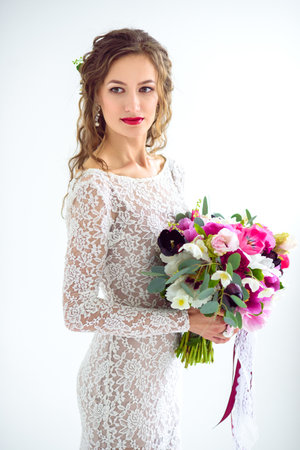joyful girl bride in a white knitted dress posing with a bouquet of flowers in the studio on a white backgroundの写真素材