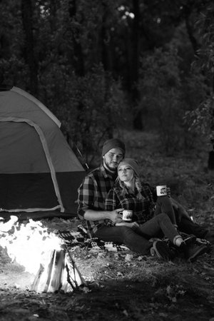 Young couple a guy and a girl in bright knitted hats stopped at a camping near the fireの写真素材