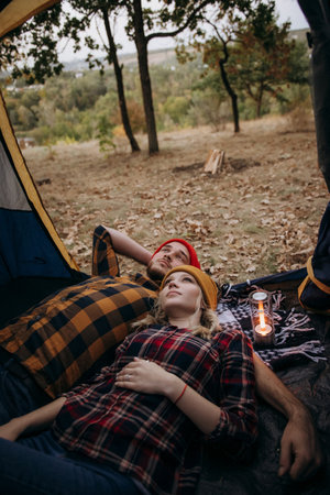 Young couple a guy and a girl in bright knitted hats stopped at a camping near the fireの写真素材