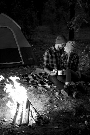 Young couple a guy and a girl in bright knitted hats stopped at a camping near the fireの写真素材