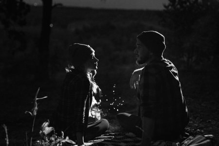 Young couple a guy and a girl in bright knitted hats stopped at a camping near the fireの写真素材