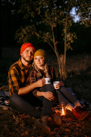 Young couple a guy and a girl in bright knitted hats stopped at a camping near the fireの写真素材