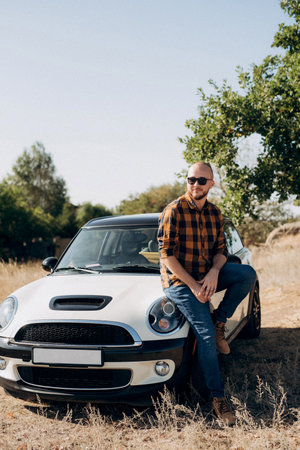 Guy in a plaid shirt next to a white car in natureの写真素材