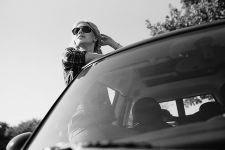 blonde with pigtails in a shirt, jeans, red shoes and black glasses near a white car