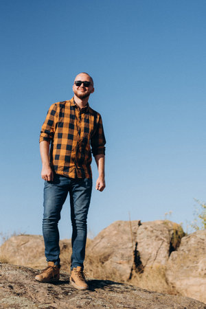 bald guy with a beard in jeans warm shirt and trekking shoes on granite rocksの写真素材