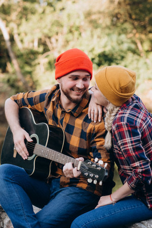 a guy in a bright hat plays the guitar with a girl against a background of granite rocks and a riverの写真素材