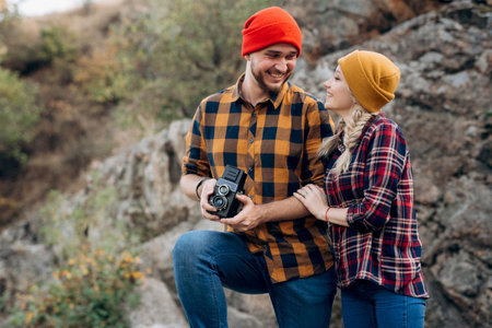 Bald guy with a beard and a blonde girl in bright hats on the background of the river are taking pictures with an old cameraの写真素材