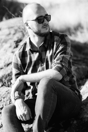 bald guy with a beard in jeans warm shirt and trekking shoes on granite rocksの写真素材
