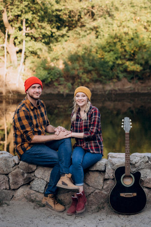 a guy in a bright hat plays the guitar with a girl against a background of granite rocks and a riverの写真素材