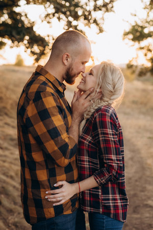 Cheerful guy with a board and a blonde girl for a walk in plaid shirts at sunsetの写真素材