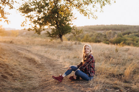 blonde with pigtails in a shirt, jeans, red shoes smiling at sunsetの写真素材