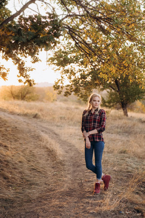 blonde with pigtails in a shirt, jeans, red shoes smiling at sunsetの写真素材