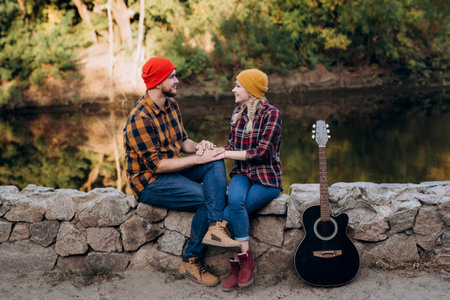 a guy in a bright hat plays the guitar with a girl against a background of granite rocks and a riverの写真素材