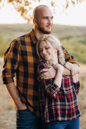 Cheerful guy with a board and a blonde girl for a walk in plaid shirts at sunsetの写真素材