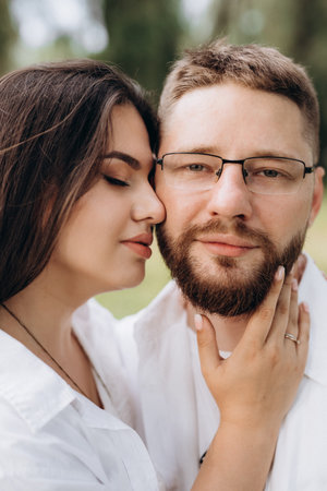 young couple in love a guy with a beard and a girl with dark hair in light clothes in the green forestの写真素材