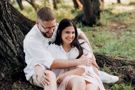young couple in love a guy with a beard and a girl with dark hair in light clothes in the green forestの写真素材