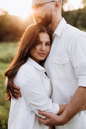 young couple in love a guy with a beard and a girl with dark hair in light clothes in the green forestの写真素材