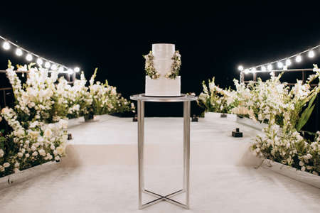 wedding white cake on a high stand near the white podium with green decorの写真素材