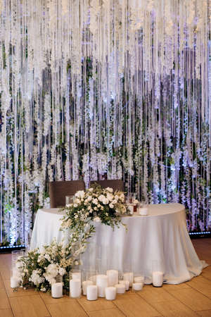 The presidium of the newlyweds in the banquet hall of the restaurant is decorated with candles and green plants, wisteria hangs from the ceilingの写真素材