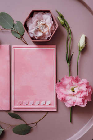 pink wedding invitation in a gray envelope on a table with green sprigsの写真素材