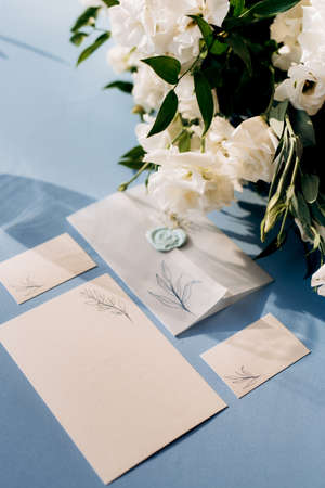 wedding invitation in a blue envelope on a table with green sprigsの写真素材