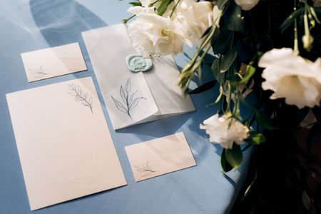 wedding invitation in a blue envelope on a table with green sprigsの写真素材