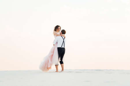 young couple a guy in black breeches and a girl in a pink dress are walking along the white sand of the desertの写真素材