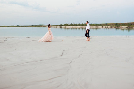young couple a guy in black breeches and a girl in a pink dress are walking along the white sand of the desertの写真素材