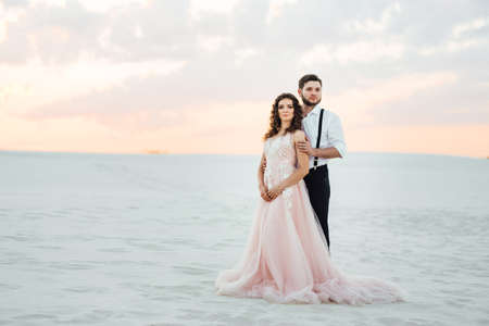 young couple a guy in black breeches and a girl in a pink dress are walking along the white sand of the desertの写真素材