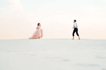 young couple a guy in black breeches and a girl in a pink dress are walking along the white sand of the desertの写真素材