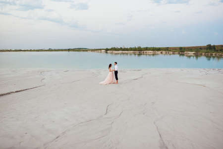 young couple a guy in black breeches and a girl in a pink dress are walking along the white sand of the desertの写真素材