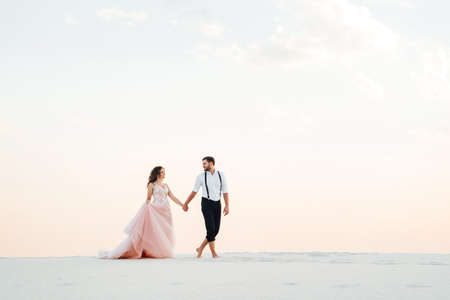 young couple a guy in black breeches and a girl in a pink dress are walking along the white sand of the desertの写真素材