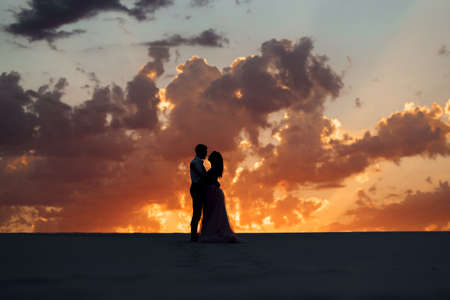 young couple a guy in black breeches and a girl in a pink dress are walking along the white sand of the desertの写真素材