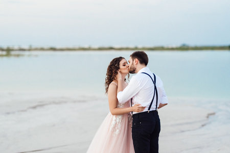 young couple a guy in black breeches and a girl in a pink dress are walking along the white sand of the desertの写真素材