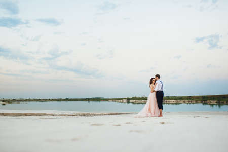 young couple a guy in black breeches and a girl in a pink dress are walking along the white sand of the desertの写真素材