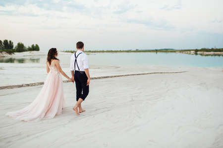 young couple a guy in black breeches and a girl in a pink dress are walking along the white sand of the desertの写真素材