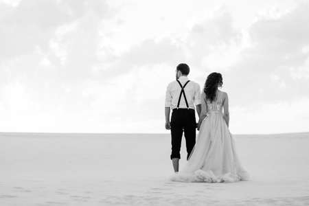 young couple a guy in black breeches and a girl in a pink dress are walking along the white sand of the desertの写真素材