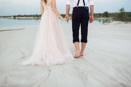 young couple a guy in black breeches and a girl in a pink dress are walking along the white sand of the desertの写真素材