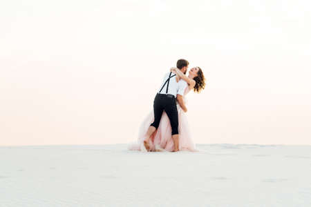 young couple a guy in black breeches and a girl in a pink dress are walking along the white sand of the desertの写真素材