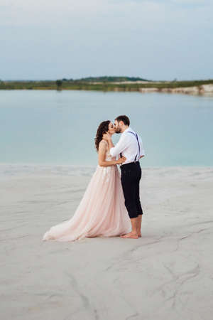 young couple a guy in black breeches and a girl in a pink dress are walking along the white sand of the desertの写真素材