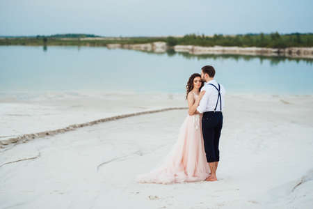 young couple a guy in black breeches and a girl in a pink dress are walking along the white sand of the desertの写真素材